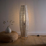 Decorative floor lamp with intricate design next to a vase on a wooden floor.